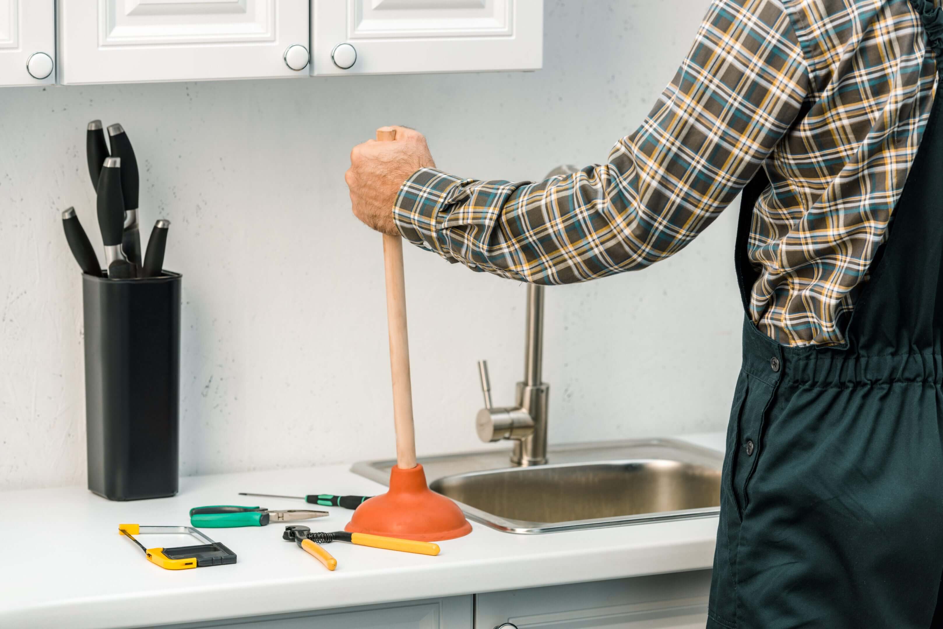 Person using plunger in kitchen sink.