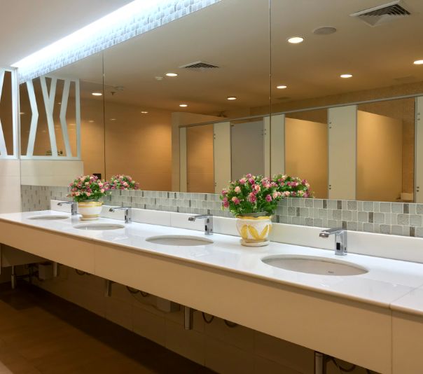 Modern public restroom sinks with floral arrangements and mirrors.
