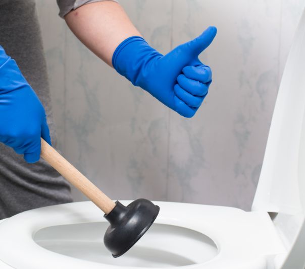Person wearing blue gloves using a plunger on a sink drain.