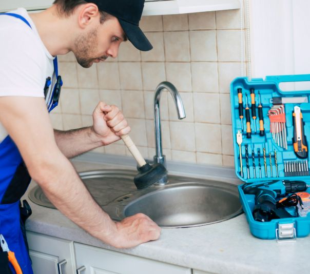 A plumber fixing a kitchen sink with tools.
