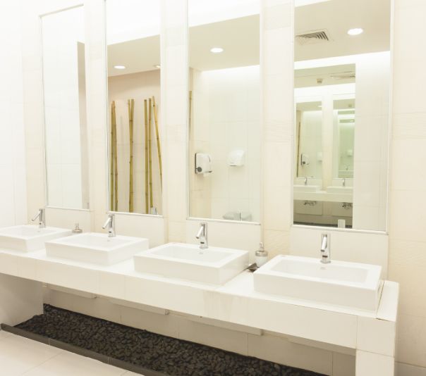 Modern public restroom with three sinks and large mirrors.