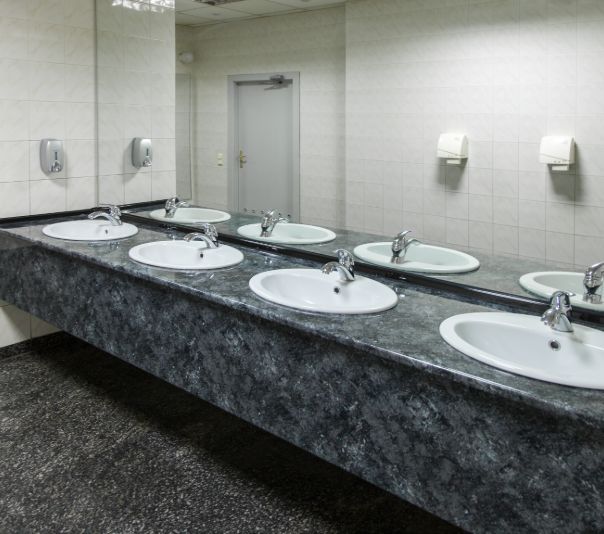A row of sinks in a public restroom with a marble countertop.