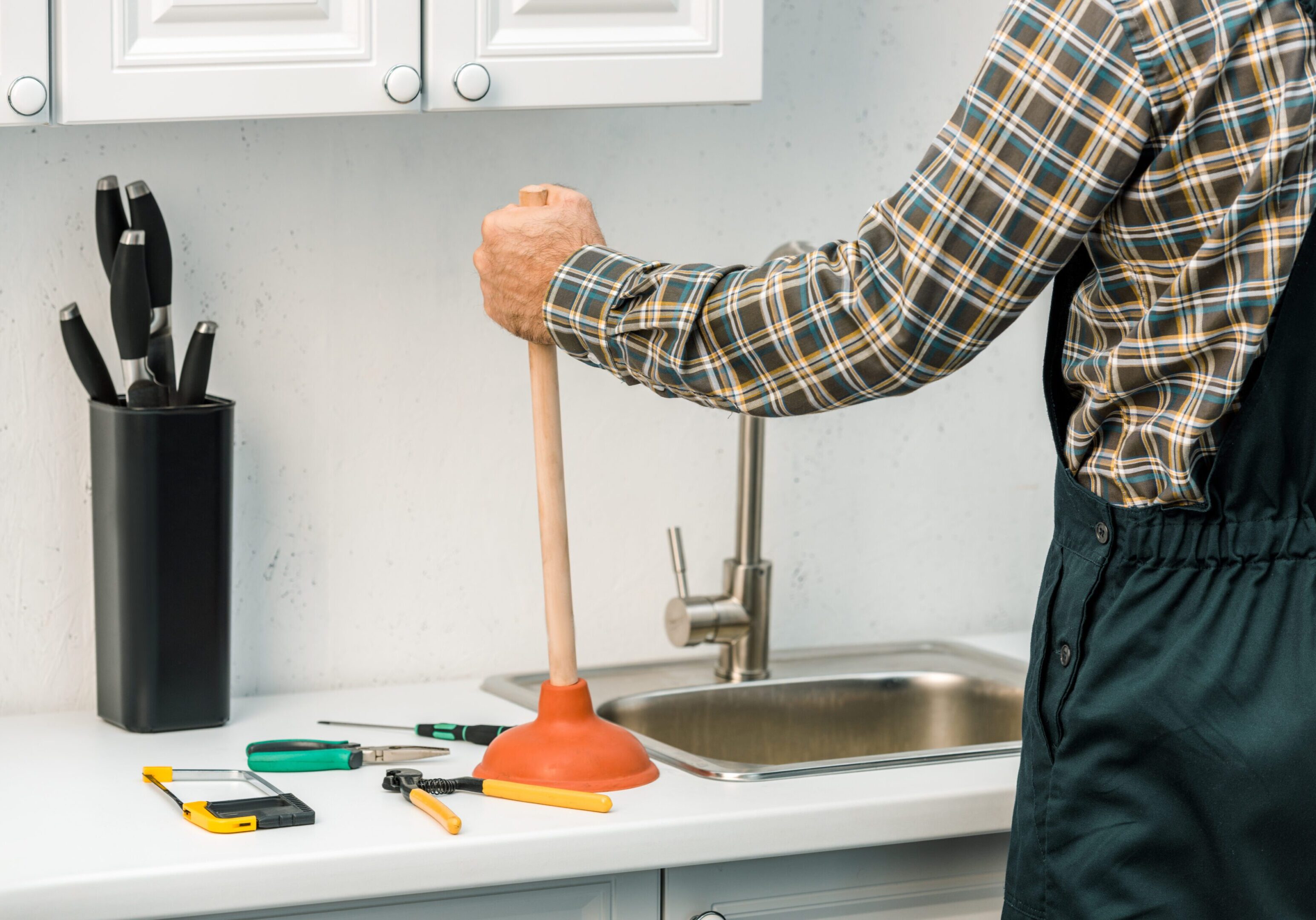 Person using plunger in kitchen sink.